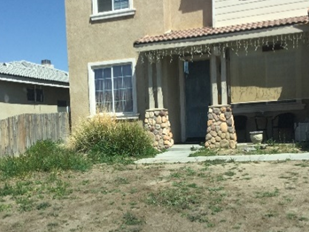 A HOUSE WITH AN UNMANTAINED FRONT YARD LANDSCAPE WITH AN OVERGROWN WEEDS VIOLATION.