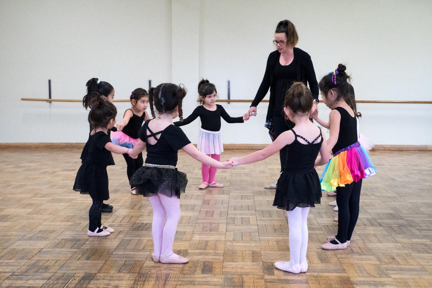 Young dance students standing in a circle with their dance teacher.