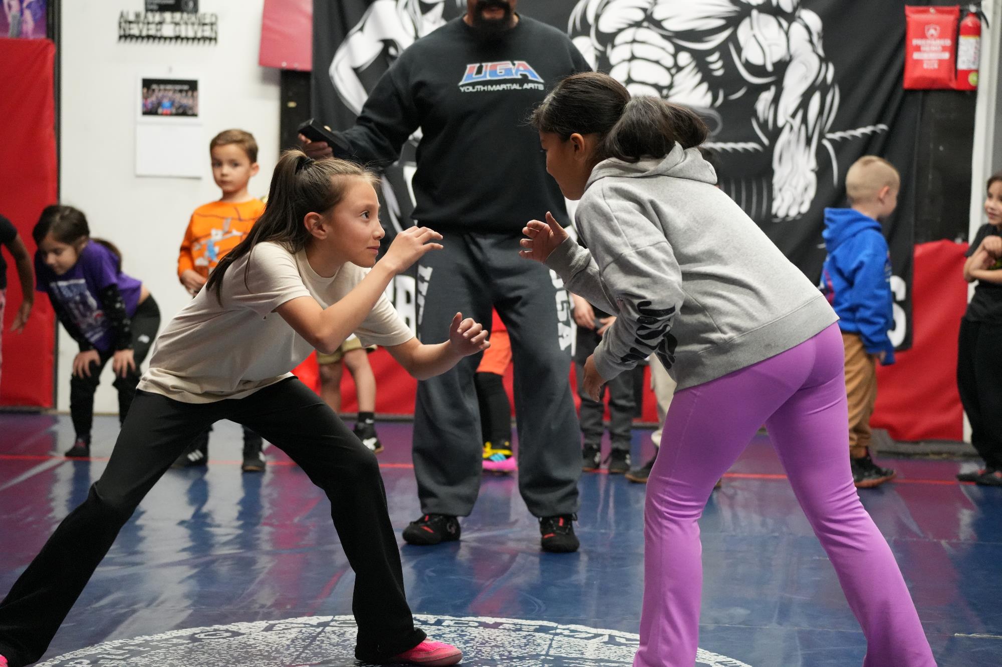 A group of children on a gym mat preparing to spar with an instructor next to them.