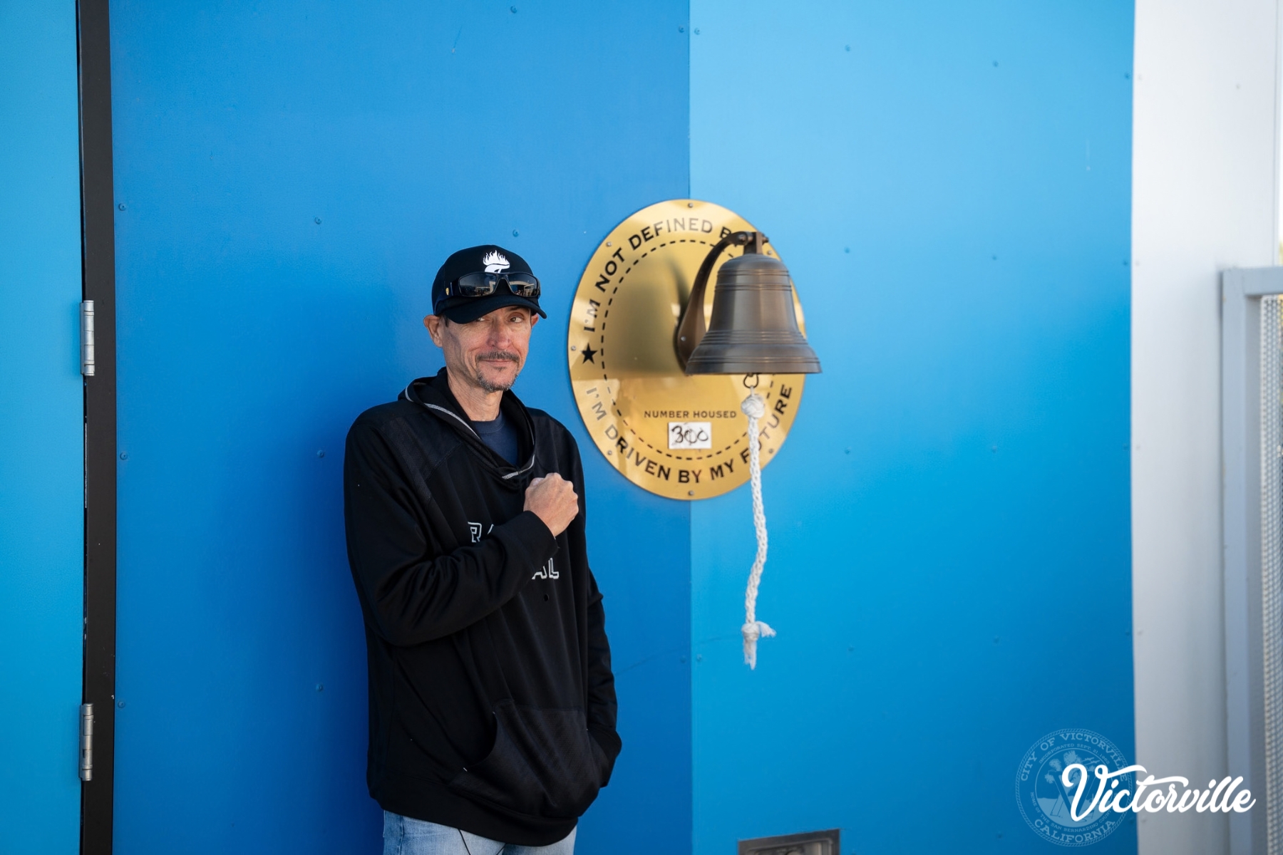 Justin D., the 300th client of Victorville's Wellness Center to graduate to permanent housing is pictured next to the celebration bell clients ring upon graduation.