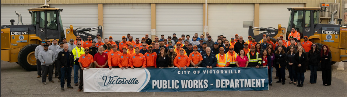 Public works staff holding a sign that says City of Victorville Public Works Department with two tractors behind them