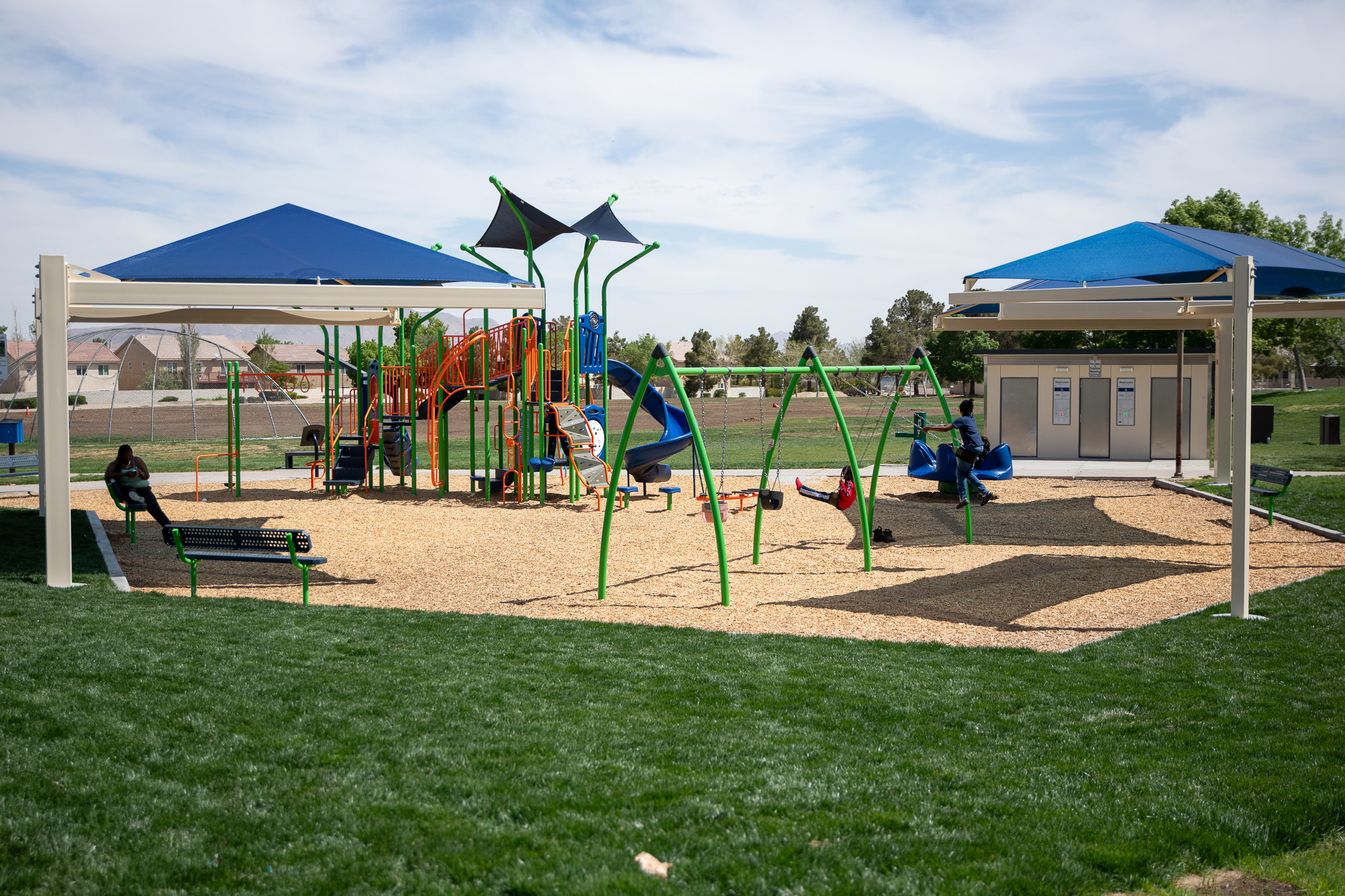 Bright green grass, swing set, bright colored slide and a shade structure at Victorville's Brentwood Park.