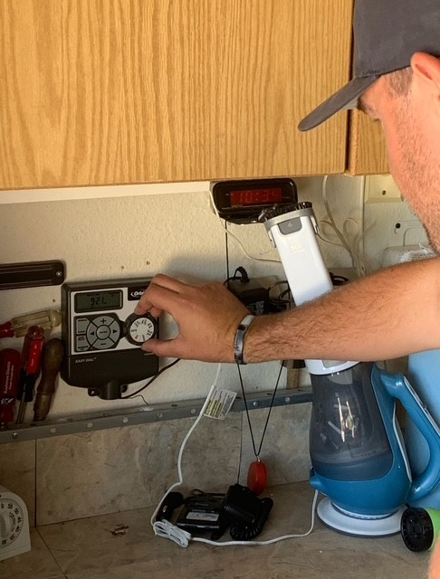 Man adjusting a wall-mounted irrigation or sprinkler control panel in a kitchen or utility area.